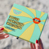 A hand holding a box of FRSHN UP's Deluxe Lightening Whitening Kit - Original Formula, showcasing its colorful packaging design.