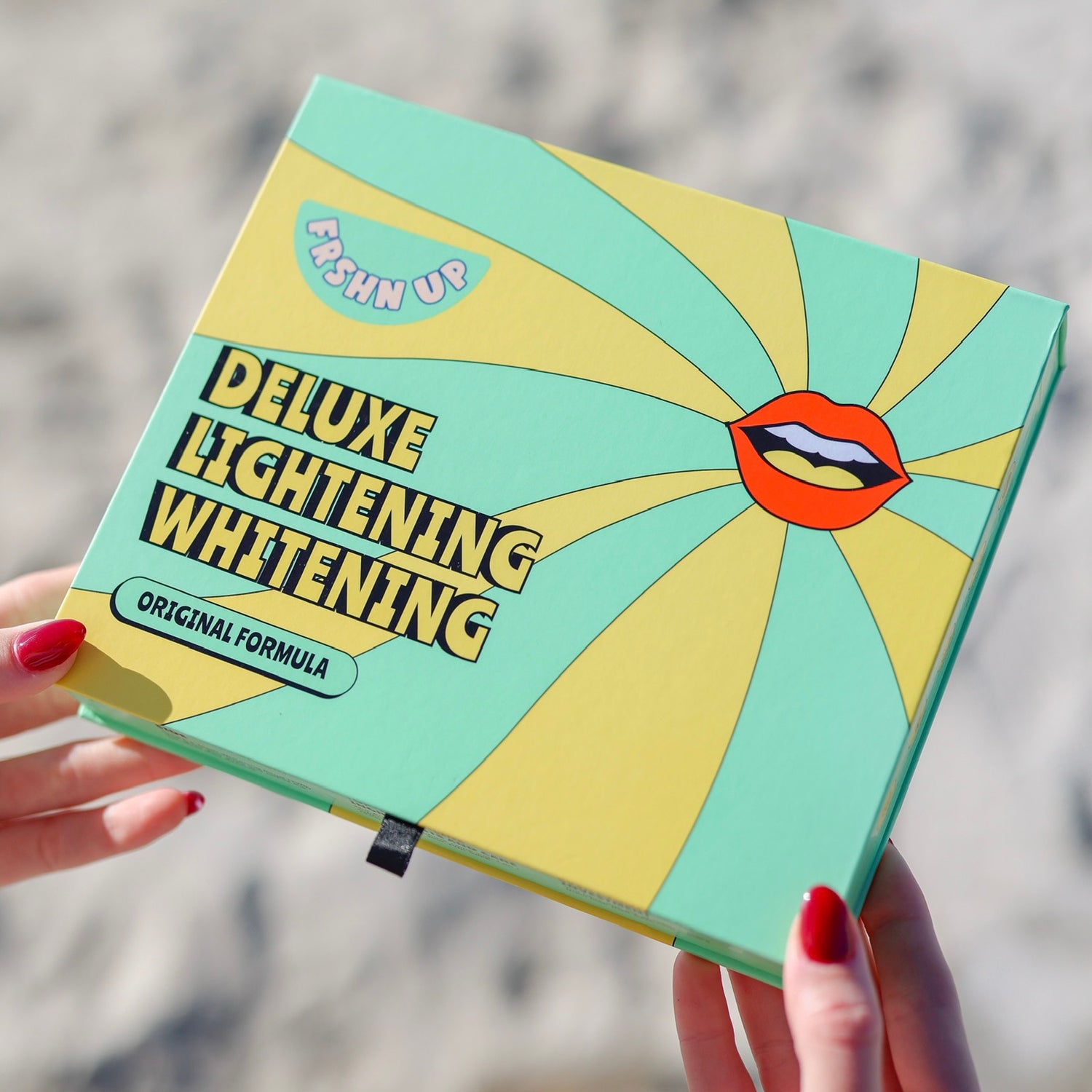 A person holds a green and yellow box labeled "Deluxe Lightening Whitening Kit" with a graphic of lips and the words "FRSHN UP" and "Original Formula" highlighting its teeth whitening power using pro-grade ingredients.