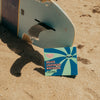 A sensitivity-free surfboard laying on the sand next to a FRSHN UP Deluxe Lightening Whitening Kit - Gentle Formula.